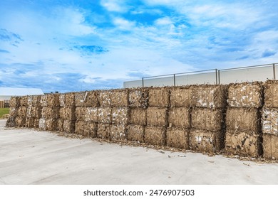 Large bales of compressed cardboard ready for recycling, stored outside a recycling plant - Powered by Shutterstock