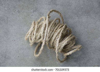 A Large Ball Of Twine That Is Partially Unraveled Sits On A Concrete Background.