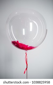 Large balloon with red feather inside hangs on white background