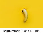 A large banana curved downward through a torn hole in yellow paper. Tropical fruit, vegetarianism. Bright background with copy space. The concept of impotence, erectile dysfunction, joke.