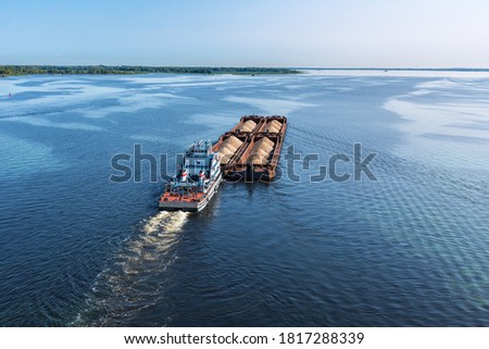 A large barge with sand sails along the coast along the wide Volga river