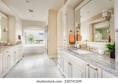 Large Bathroom Interior In Luxury Home With Two Sinks, Tile Floors, Fancy Cabinets, Large Mirrors, And Bathtub