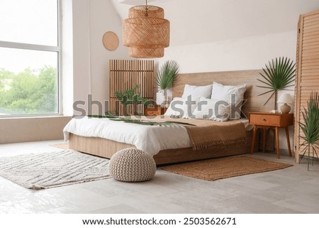 Large bed, bedside tables and pouf decorated with palm branches in bedroom