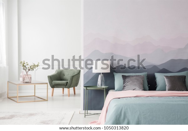Large bed with blue\
sheets and a pink blanket by a landscape wallpaper in a cozy,\
modern bedroom interior