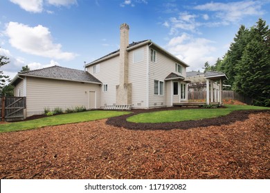 Large Beige House With Empty Backyard During Spring With Mulch And Grass.