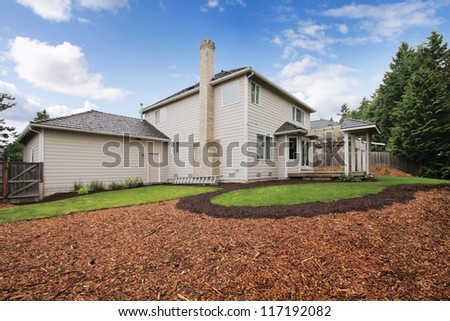 Large beige house with empty backyard during spring with mulch and grass.
