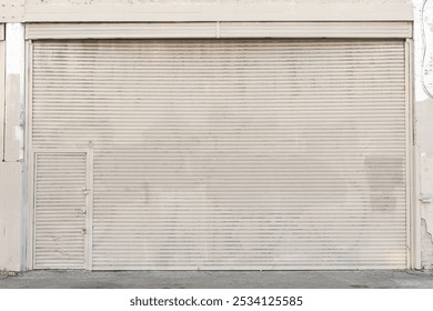 Large beige rolling shutter with subtle wear and a pedestrian door embedded, showcasing industrial design and urban functionality.