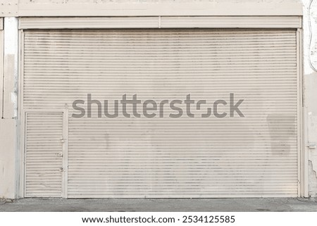 Large beige rolling shutter with subtle wear and a pedestrian door embedded, showcasing industrial design and urban functionality.