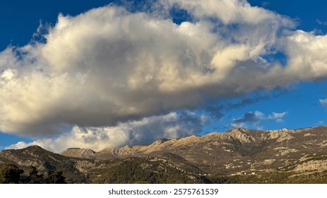 Large, billowing clouds hover above a rugged mountain range as golden sunlight illuminates the peaks.