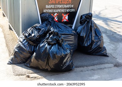 large black bags of garbage near the dumpster (inscription in Russian - the RELEASE OF CONSTRUCTION AND LARGE-SIZED GARBAGE is PROHIBITED)