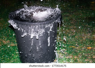 A large black bin overflows with rain water from a tropical storm