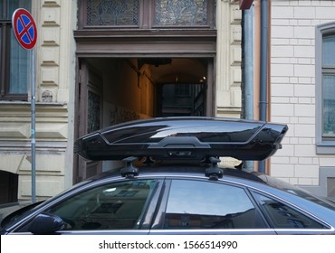 Large Black Box Trunk On The Roof Of A Dark Modern Car. Travel And Accessories For Transportation. Trunk Box Fixed At Roof Top Of The Car