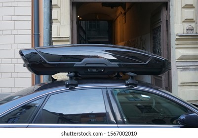 Large Black Box Trunk On The Roof Of A Dark Modern Car. Travel And Accessories For Transportation. Trunk Box Fixed At Roof Top Of The Car