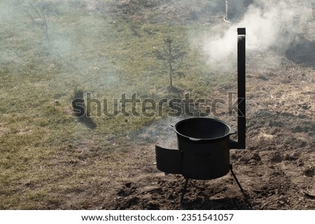 A large black tourist pot is cauldron over a burning flame of a fire in a forest in a furnace. Cooking dinner on a wild hike in the fresh air. A cauldron of hot food is heated on fire. Outdoor travel.