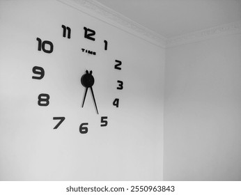 A large, black wall clock mounted on a white wall in the corner of a room. The clock is modern and minimalist in design, with simple black numbers and hands - Powered by Shutterstock