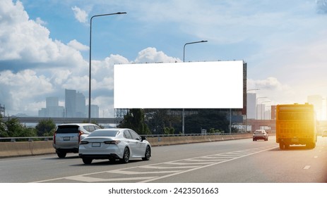 A large, blank billboard on the side of a highway. The billboard is white. It is located in a rural area, with trees and grass in the background. The sun is shining and the sky is blue, clipping path. - Powered by Shutterstock