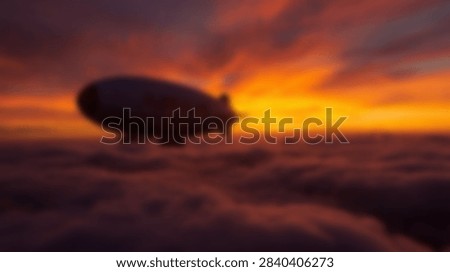 A large blimp or dirigible gracefully navigates the vibrant sky during a breathtaking sunset, casting a silhouette against the fiery clouds.