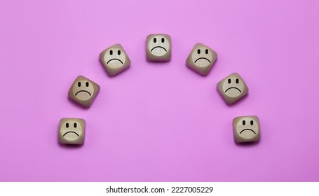 Large block cubes with sad faces on a pink background, depicting feelings of sadness and unwelcomeness. Includes free space for text or messaging.
