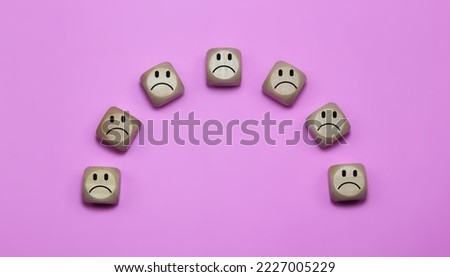 Large block cubes with sad faces on a pink background, depicting feelings of sadness and unwelcomeness. Includes free space for text or messaging.