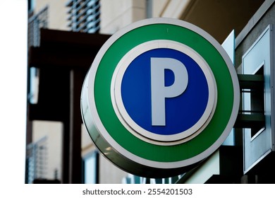 A large blue and green circular "P" sign signifying a public parking garage, attached to a wall of a building in urban area, illuminated at night - Powered by Shutterstock