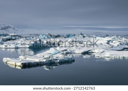 Large blue ice blocks drift through the fast-moving glacial channel at Jokulsarlon Glacier Lagoon in Iceland, surrounded by snowy shores and distant mountains during winter.
