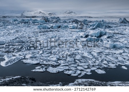 Large blue ice blocks drift through the fast-moving glacial channel at Jokulsarlon Glacier Lagoon in Iceland, surrounded by snowy shores and distant mountains during winter.