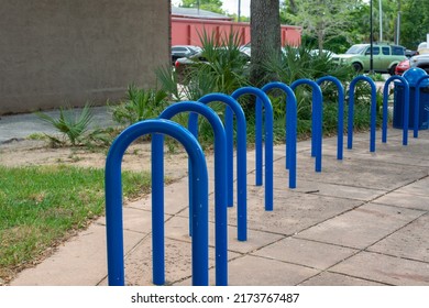 Large blue metal bicycling hub racks. The curved wave shape of the metal stands is attached to the edge of a brick foundation patio. The commercial short term u bike rack for multiple bikes. 