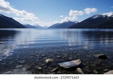 A large body of water surrounded by mountains under a blue sky with cloudsa