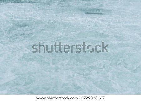 A large body of water with a lot of waves. The water appears to be very cold and choppy, with a lot of foam and spray. Scene is one of power and energy