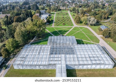 A large botanical garden features a prominent glass greenhouse with geometric design, surrounded by symmetrical pathways, lush greenery, and urban backdrop. - Powered by Shutterstock