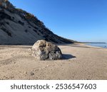 Large boulder on beach by sand cliff bluff under blue sky