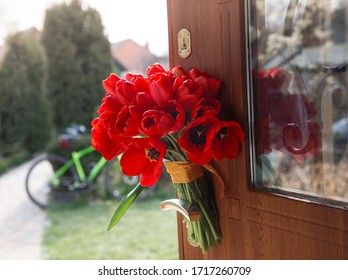 large bouquet of red tulips on the handle of the front door. Surprise, a pleasant unexpected gift, a sign of attention, gratitude. In the background a bicycle in defocus. Sunny spring holiday