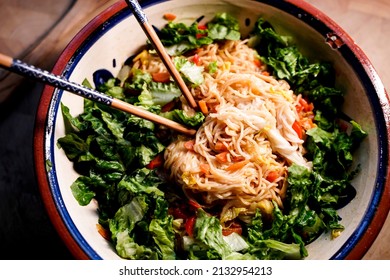 A Large Bowl Of Asian Noodles And Fresh Salad And Chopsticks To Eat.