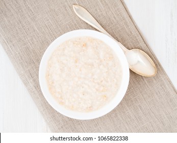 Large bowl of tasty and healthy oatmeal for Breakfast, morning meal. Top view, close up, white wooden rustic table.