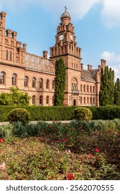 A large brick building with a clock tower and a courtyard with flowers. The building is old and has a lot of history