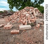 A large brick building has just been demolished. A pile of red bricks and debris are stacked in a pile of debris. Large demolition construction site.