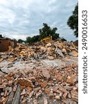 A large brick building has just been demolished. A pile of red bricks, wood insulation and debris are stacked in a pile. Bulldozer in background of view. Large demolition construction site.