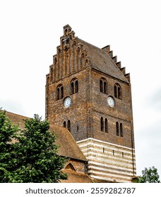 A large brick tower with a clock on it. The clock is located on the side of the tower. The tower is tall and has a pointed top. The sky is cloudy and the sun is not visible