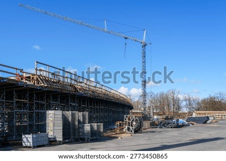 Large bridge construction site with tower crane, scaffolding and concrete overpass structure under bright blue sky outdoors