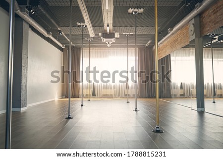 Large bright room with vertical poles for dancing, big mirrors and window with curtains
