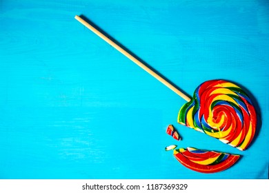 large broken multi colored striped lollipop on blue wood background