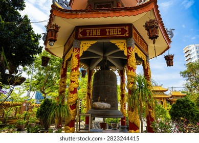 A large bronze bell hangs inside an ornate Buddhist pavilion featuring golden dragon carvings and traditional lanterns in Da Nang, Vietnam. Da Nang, Vietnam