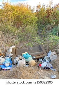 Large brown sofa, soft teddy bear are thrown out in trash heap in summer outdoors. Pollution of nature, environment, garbage. Poor ecology in Cyprus, Paphos city. Stuffed animals are thrown away.
