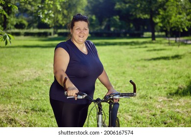 Large Build Caucasian Woman Rides A Bicycle In The Park On A Sunny Summer Day.