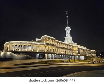 Large building with a clock tower and a statue on top. The building River port is lit up at night in Moscow