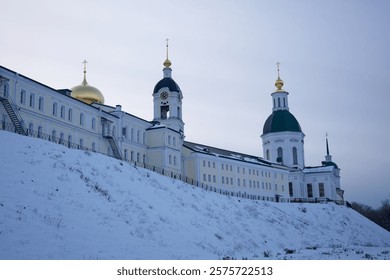 Large building with two domes and a clock tower. The building is surrounded by snow and he is a church. The monastery of the Sarov Desert