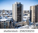 Large building with a lot of windows is seen from above. The building is surrounded by other buildings and trees. The sky is clear and the snow is covering the ground