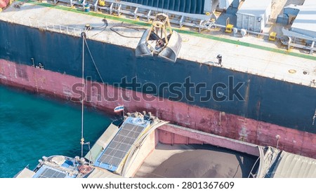 large bulk carrier ship transferring dark bulk cargo like coal or minerals into smaller barges alongside it in the open sea, representing maritime logistics and global supply chain.