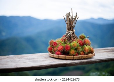 A large bunch of red rambutan in a bamboo tray is placed on a wooden table. Looks delicious to eat rambutan, fresh fruit from the tree in Thailand. Leave space for text
