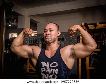 A large and burly man executes a double bicep pose at the gym. Bodybuilding subculture.